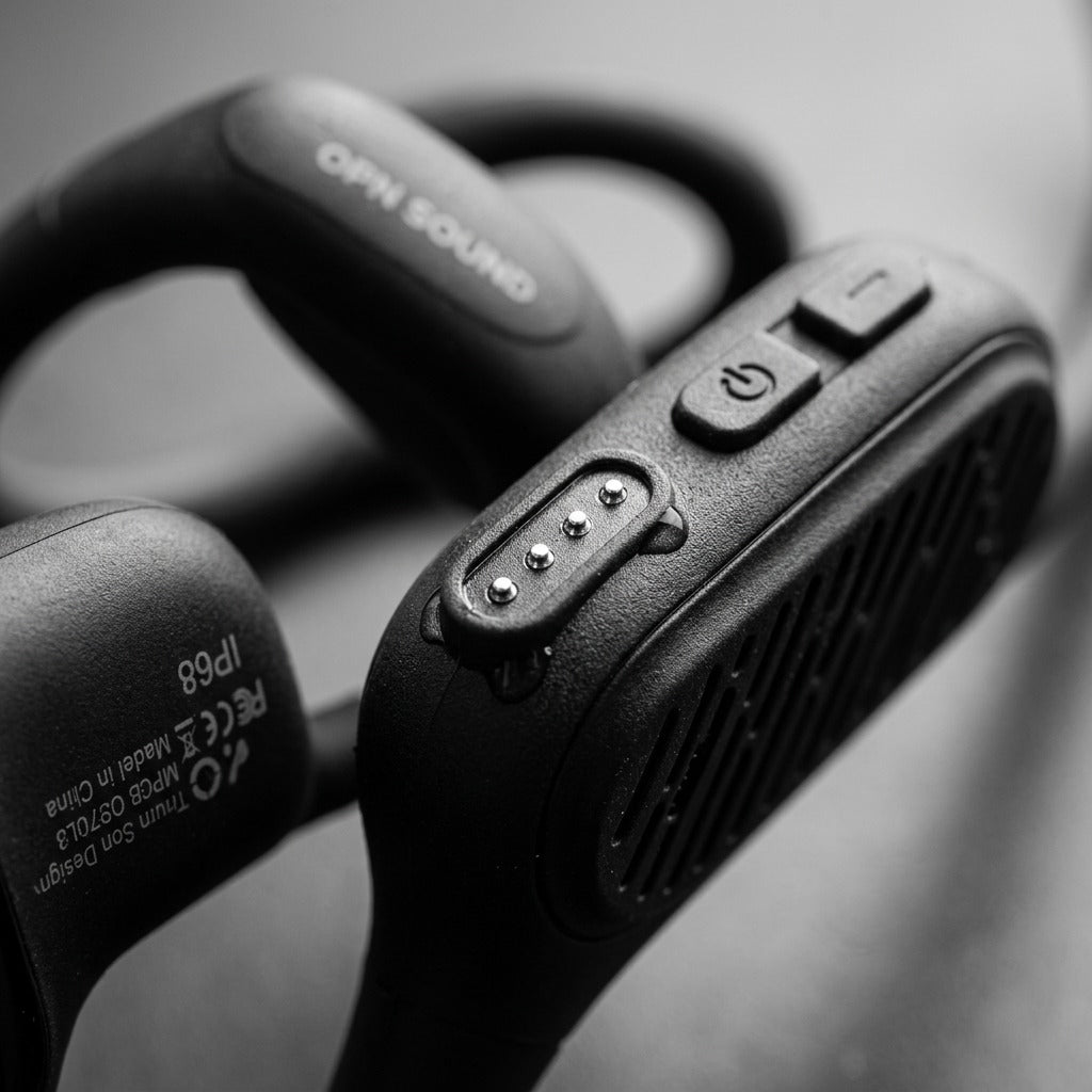 Macro detail of OPN Sound Swym+ headphones showing magnetic charging port and tactile buttons.